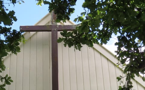 Church cross and white timber wall framed by tree canopy