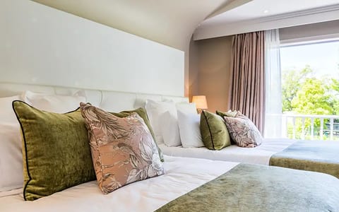 Twin hotel room with green and pink cushions, white bedding, balcony with tree view
