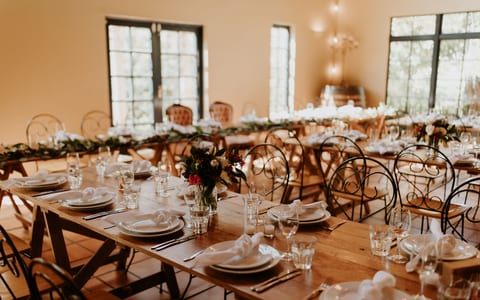 Timber trestle tables set for a reception with iron chairs and large steel-framed windows