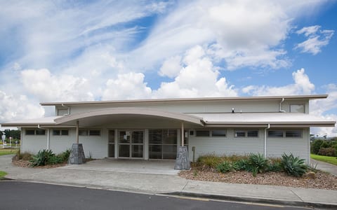Single-storey hall with curved roof canopy, corrugated cladding and planted entrance