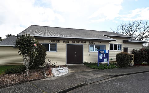 Single-storey weatherboard hall with corrugated roof and entrance garden