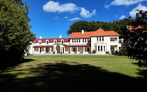 Large white rendered mansion with terracotta tile roof, columned portico, sweeping lawn