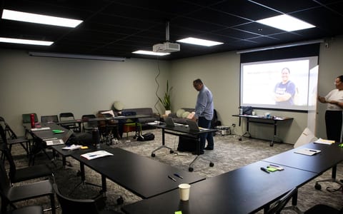 Meeting room with tables, chairs and projector screen showing presentation