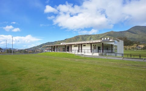 Single-storey pavilion with covered verandah, open to green sports fields and hills beyond