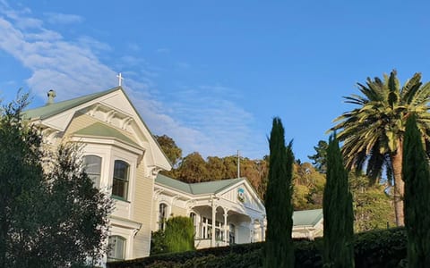 Heritage villa exterior with cross-topped gable, palm trees and gardens