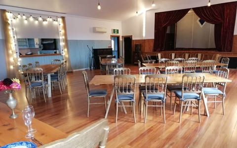 Hall interior with timber floor, dining tables with gold chairs, a bar to the left and a raised stage with red curtain