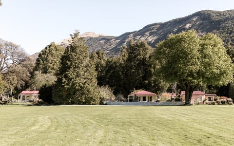 Red-roofed accommodation buildings across a wide flat lawn with mature trees and mountains behind