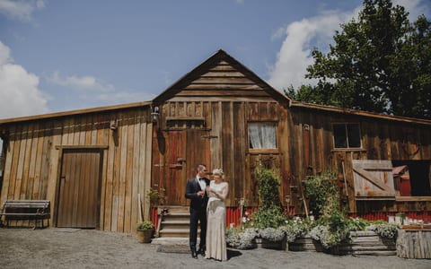Weathered timber barn with vertical board cladding, a sliding barn door and a planted front border under a blue sky