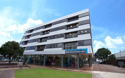 Multi-storey library building with white facade, glazed ground floor, and lawn forecourt