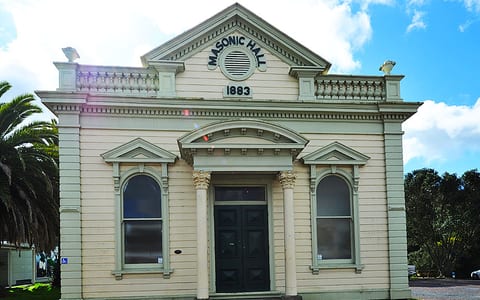 Cream weatherboard hall with classical columns, arched windows, and pediment facade dated 1883