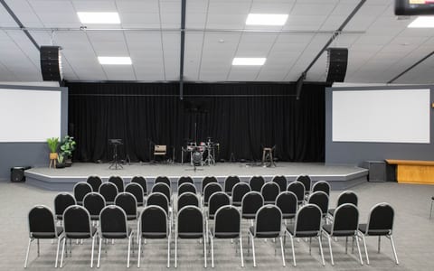 Modern church hall with rows of chairs facing a raised platform, flanked by large screens and a lighting rig