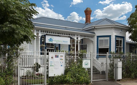 White weatherboard villa exterior with decorative veranda, metal fence, and street frontage