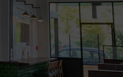 Cafe counter area with green tiled front, shelving, pendant lights, and large windows