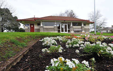 Low single-storey building with tiled roof, stone base and flower garden path