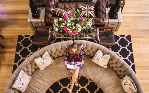 Curved tufted sofa and leather chesterfield on patterned rug, timber floor, overhead view