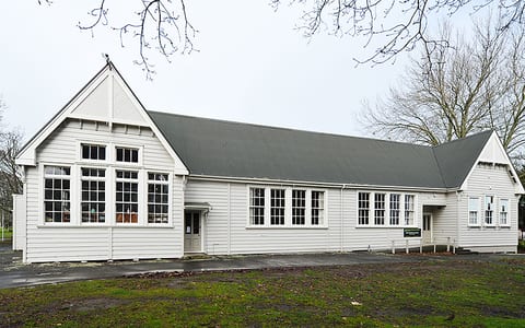 White weatherboard hall building with pitched roof and large windows