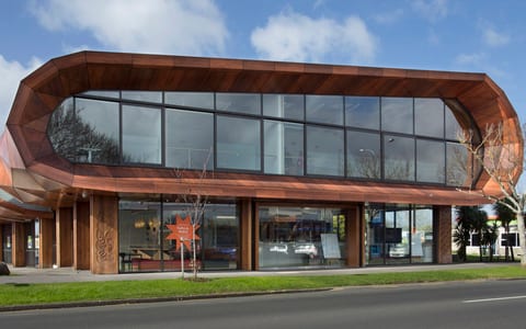Two-storey timber-clad building with curved roofline, large glazed facade, street frontage