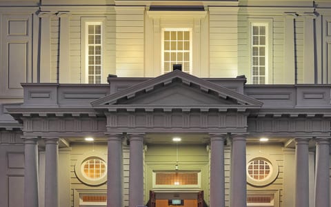 Classical portico facade with columns, triangular pediment, and round windows lit at night