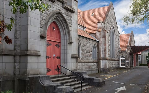 Stone Gothic church exterior with red door, arched windows, and tiled roof