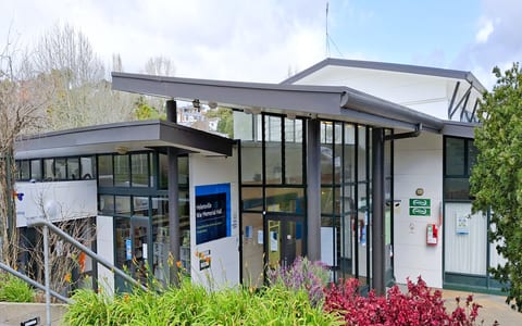 Contemporary glass-fronted community hall building with garden planting, Helensville War Memorial Hall signage visible