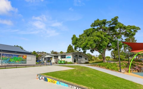 Single-storey community building and playground area with trees and shade sail