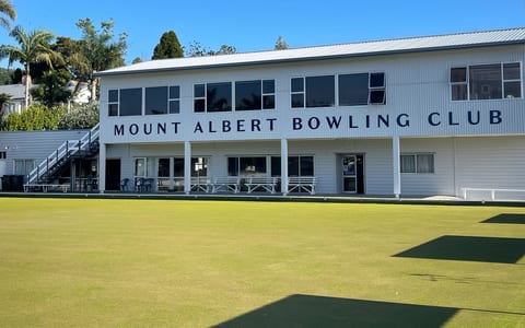 Two-storey white club building beside a flat bowling green