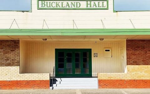 Cream and red brick hall exterior with green-trimmed entrance canopy and signage above double doors