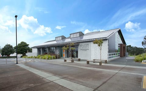 Modern library building with metal roof and decorative panel, car park in foreground
