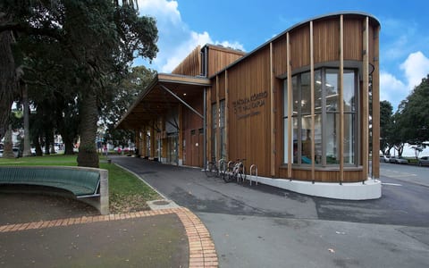 Contemporary timber-clad building with curved glass corner section, footpath and park bench in foreground