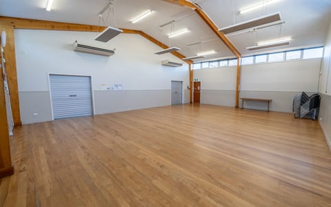 Empty hall with timber floorboards, exposed beam ceiling and roller doors on side wall