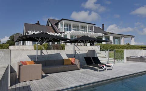 White render house with dark roof, pool terrace, deck furniture, and pergola beyond