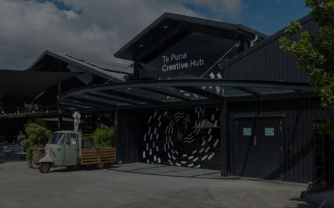Dark timber-clad building with covered entry, large spiral mural on wall, outdoor courtyard
