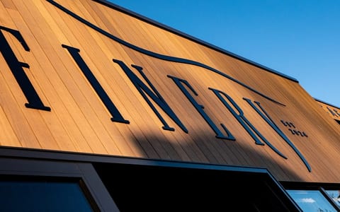 Warm timber-clad barn gable end with large cut-out signage, angular roof, clear blue sky