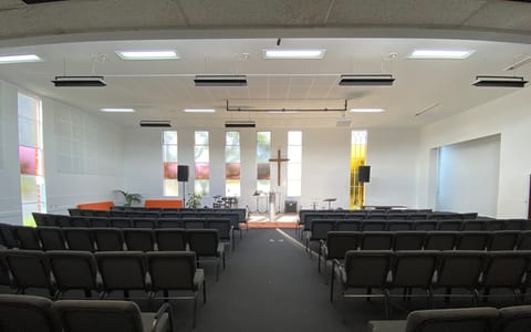 Church sanctuary with rows of chairs, cross at front and coloured window panels