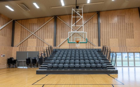 Sports hall with bleacher seating and basketball hoop on timber floor