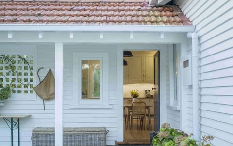 White weatherboard house with covered entry porch, terracotta tile roof and potted plants