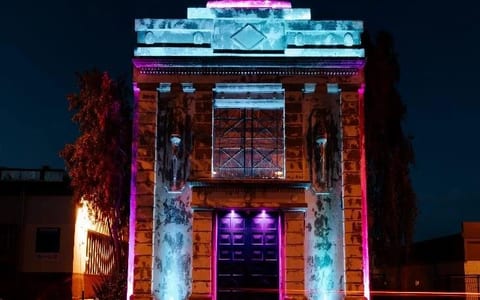 Historic stone building with classical columns lit with coloured lighting at night