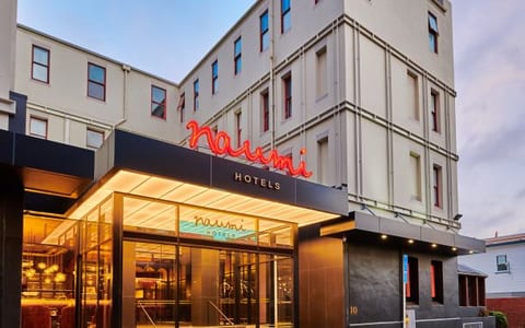 Cream multi-storey building with black canopy entrance, neon signage, street setting at dusk