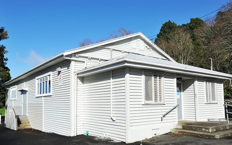 White-painted weatherboard hall building with steps and trees behind