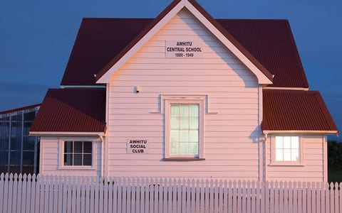 White weatherboard hall with red iron roof and picket fence, lit at dusk
