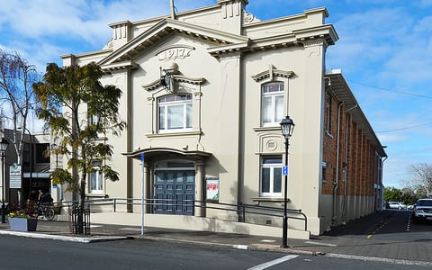 Cream rendered heritage hall with ornate parapet, arched entrance and columned porch, street corner