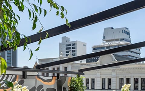 Rooftop terrace with dark sofas, orange chairs, geometric mural, and city buildings in background