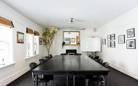 White-walled meeting room with long dark table, black chairs, fireplace and framed prints
