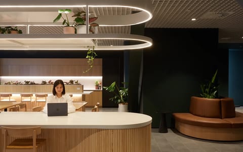Contemporary open-plan workspace with curved timber reception counter, oval pendant lights, and hanging plants