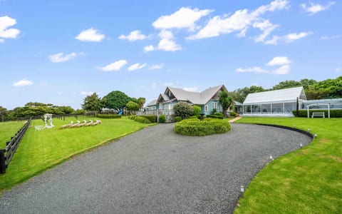 Gravel driveway curving to a dark-trimmed country house with steeply pitched roof, large lawn, white marquee to one side