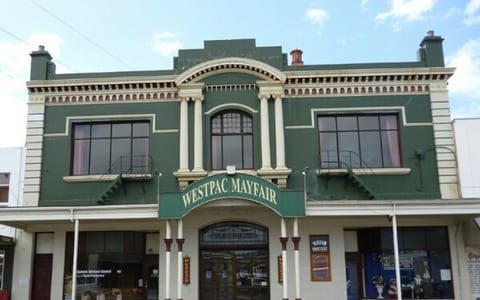 Two-storey green heritage commercial facade with white columns, arched windows, and ornate cornice