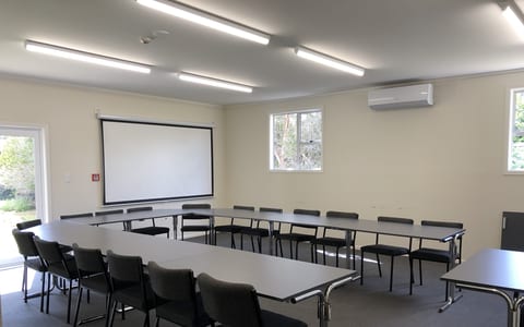 Plain meeting room with tables arranged in U-shape and projection screen