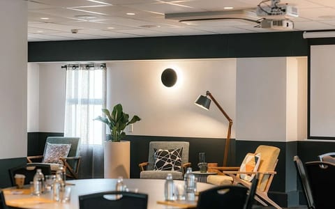 Modern breakout lounge with dark two-tone walls, mid-century chairs, floor lamp, and projector screen