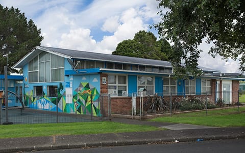 Single-storey blue community hall building with mural, fence and car park