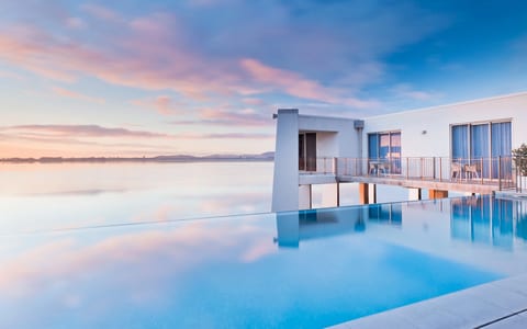 White render building with infinity pool at dusk, reflecting pink and blue sky over water